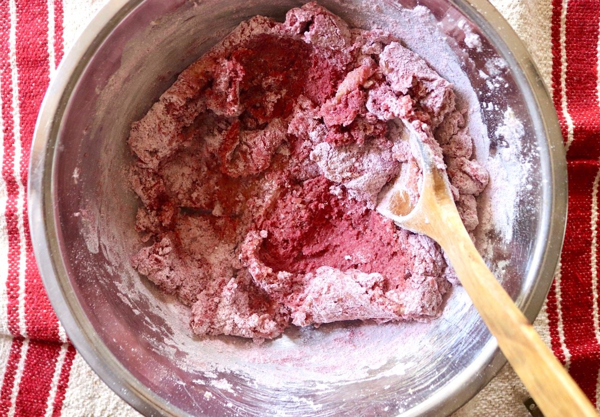 Beet cookie batter being mixed in a stainless steel bowl with a wooden spoon.