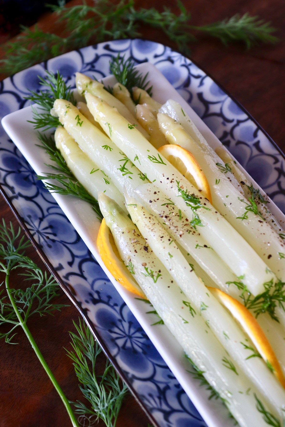 White asparagus spears on a rectangular place with fresh dill and lemon slices.