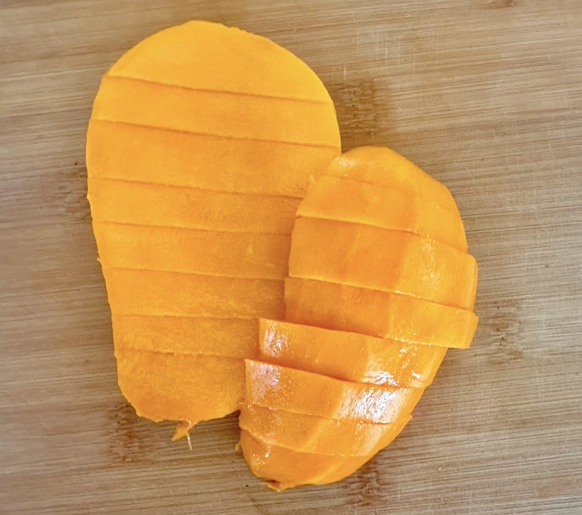 Peeled mango with several pieces cut off together in one clump, on a light wood cutting board.