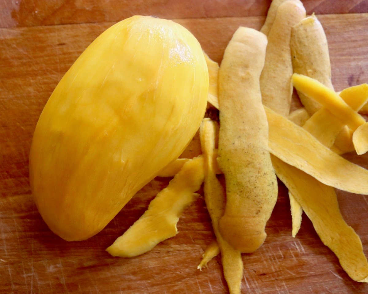 Whole peeled mango on cutting board with peels next to it.