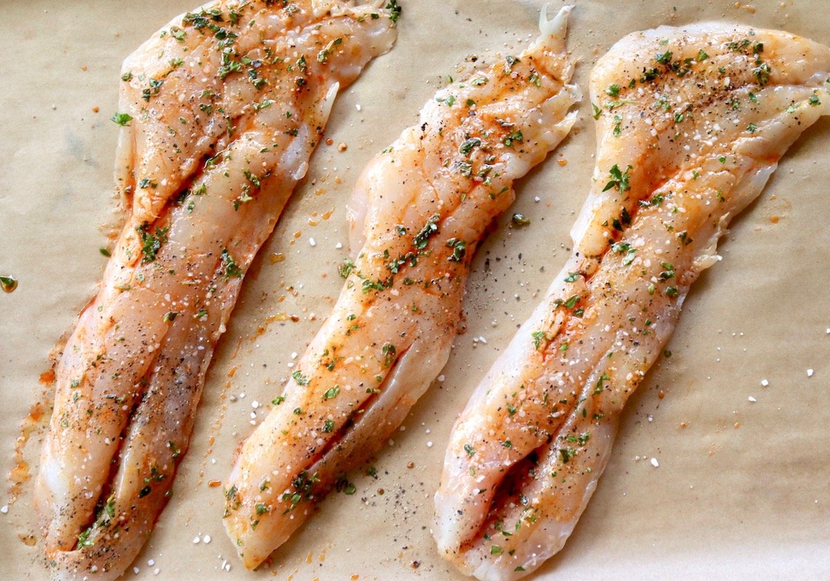 Three raw rockfish fillets with herb marinade on parchment.