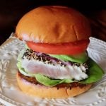 Sesame-Crusted Ahi Tuna Burger with tomato and avocado on a cream-colored plate.