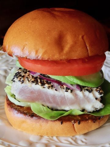 Sesame-Crusted Ahi Tuna Burger with tomato and avocado on a cream-colored plate.