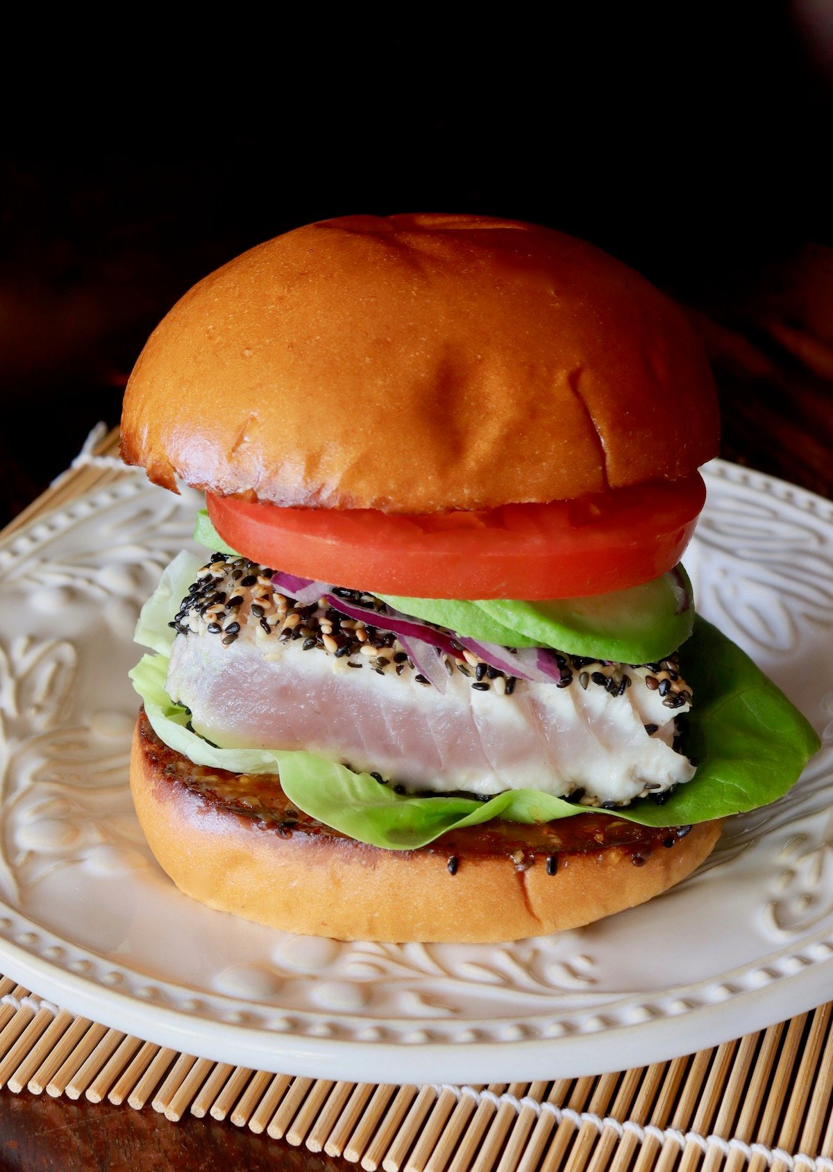Sesame-Crusted Ahi Tuna Burger with tomato and avocado on a cream-colored plate.