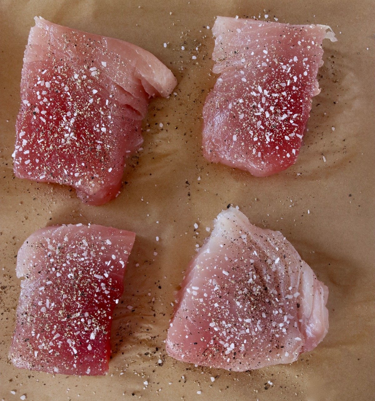 Four ahi tuna steaks seasoned with salt and pepper on parchment paper.