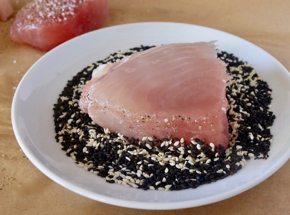 Ahi tuna steak on top of sesame seeds in a white plate.