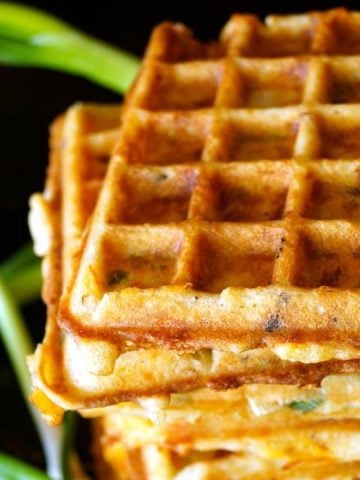 Stack of several Bacon Cheddar Waffles with fresh scallions and black background.