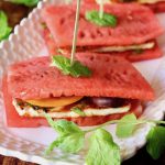 Close up of 2 watemelon Halloumi sandwiches on a white narrow plate with toothpicks and mint leaves.