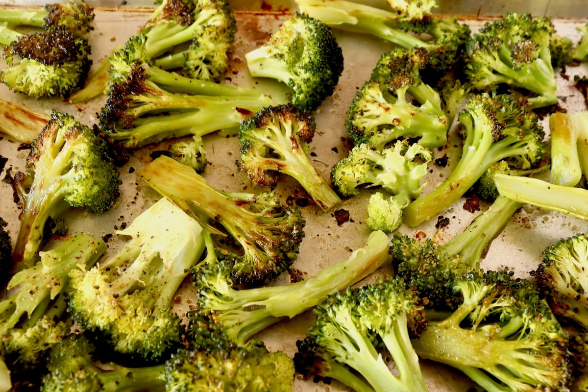 Sheet pan full of partially charred broccoli cut into bite-sized pieces.