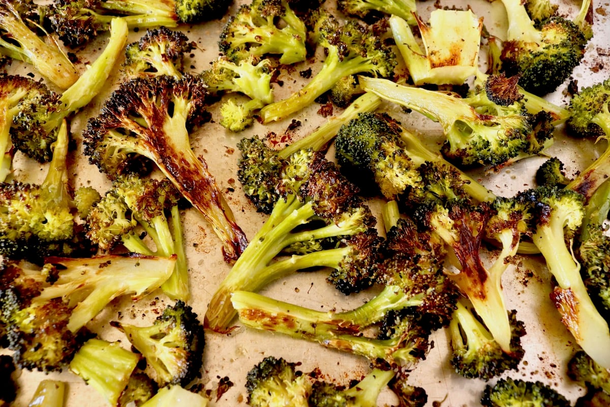 Sheet pan full of super charred broccoli cut into bite-sized pieces.