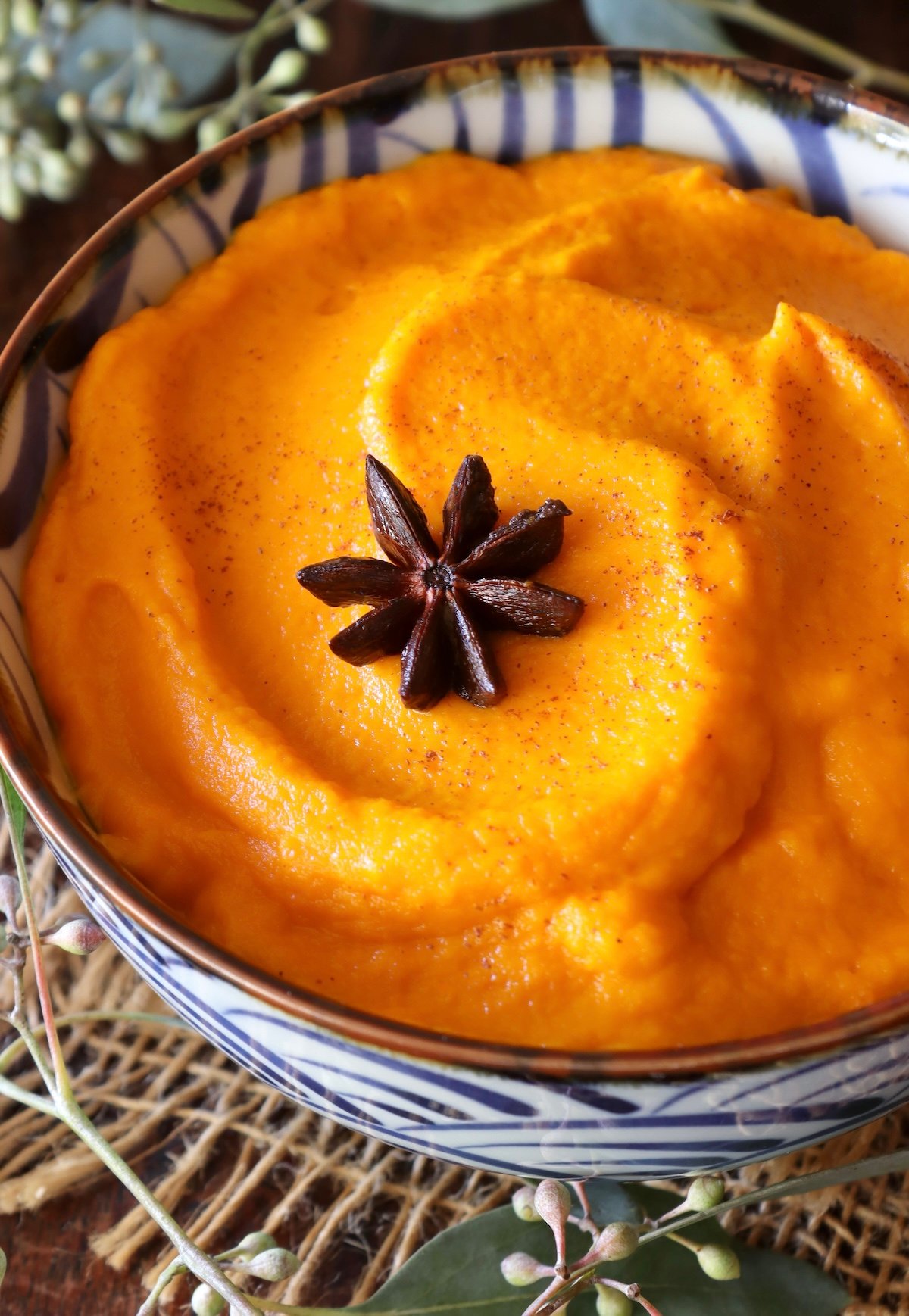 Top view of Carrot Puree in a blue and white bowl with on star anise pod on top.