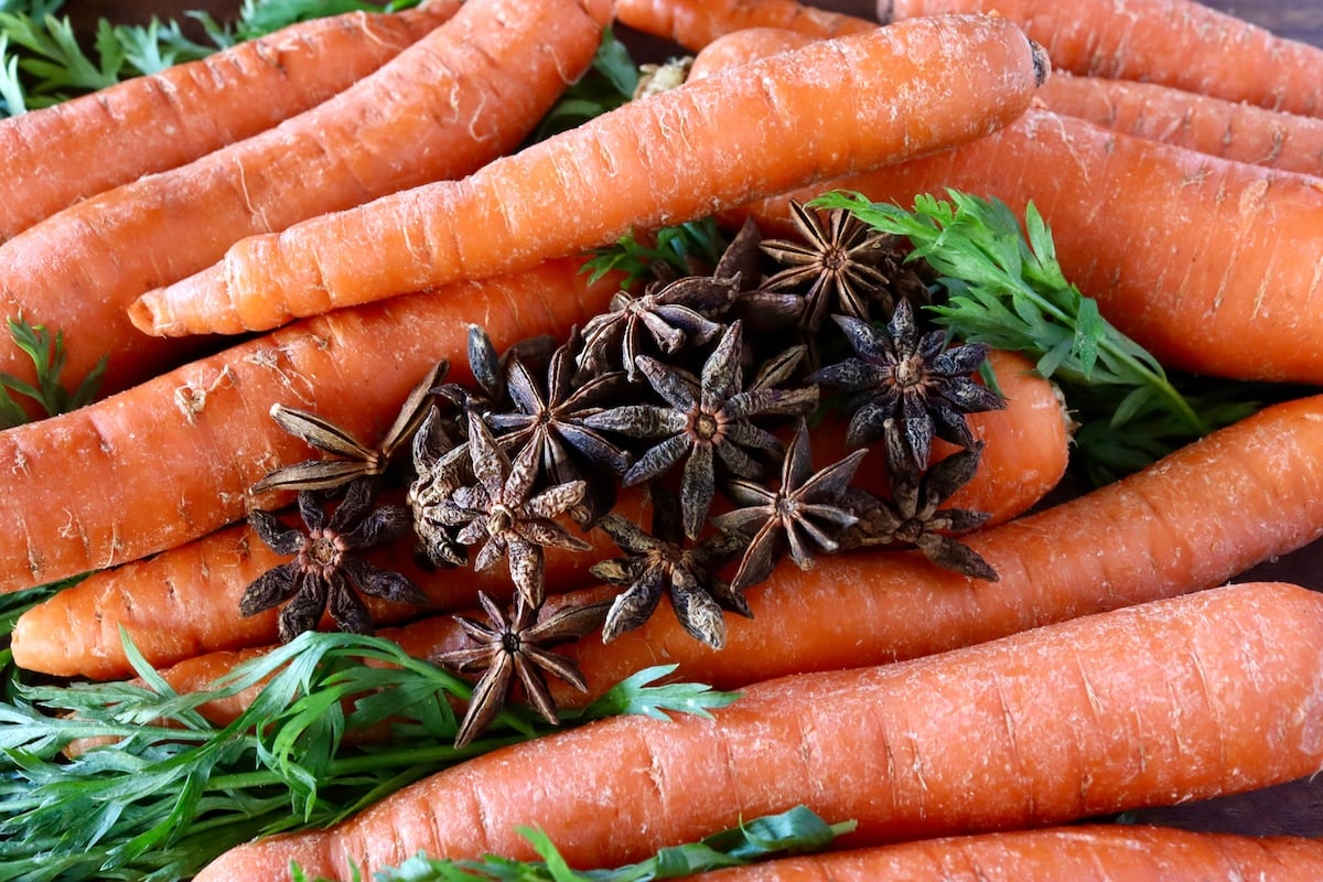 Raw, unpeeled carrots with carrot greens and a small pile of star anise on top.