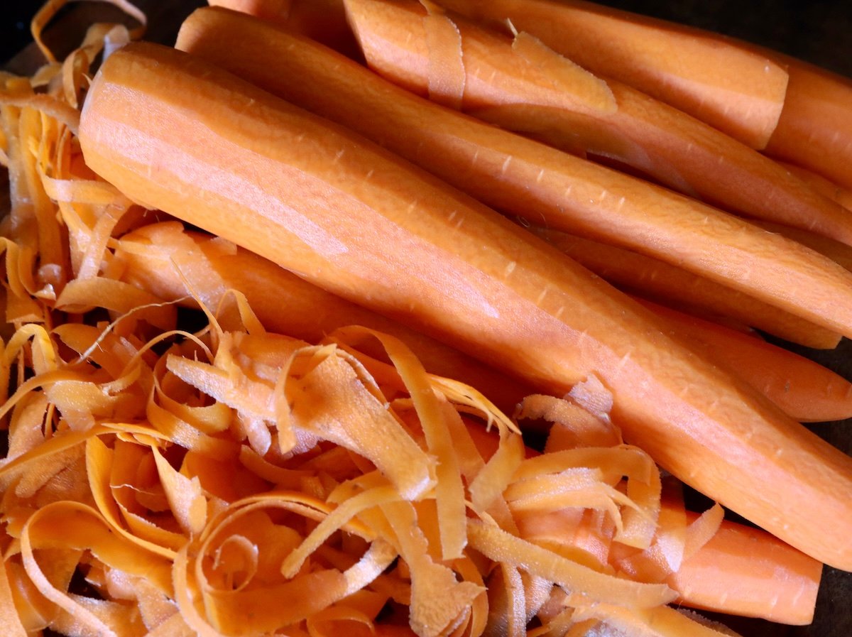 Several large, peeled carrots with peels next to them.