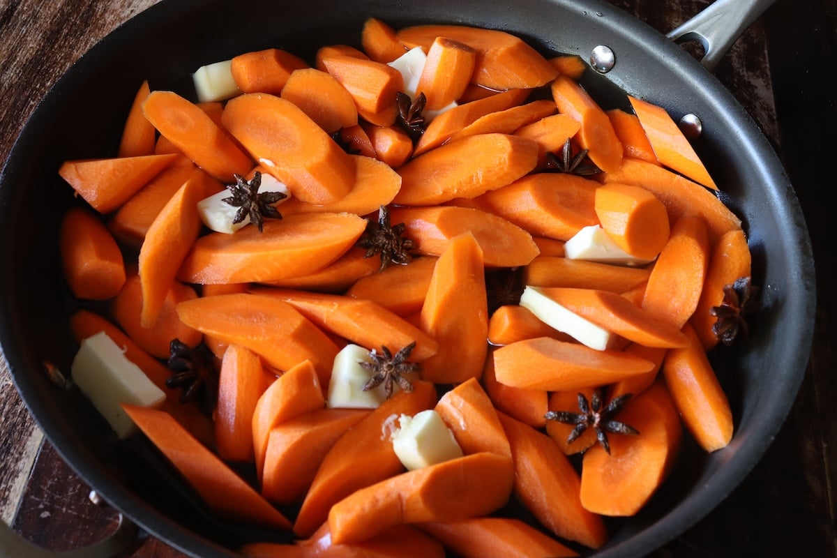 Raw carrot slices with a few pats of butter and several Star Anise, in water in a sauté pan.