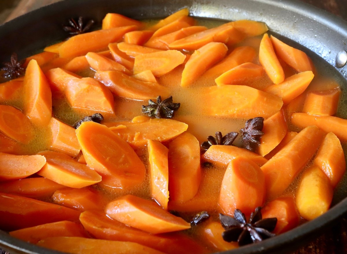 Cooked carrot slices with in buttery water and several Star Anise, in water in a sauté pan.