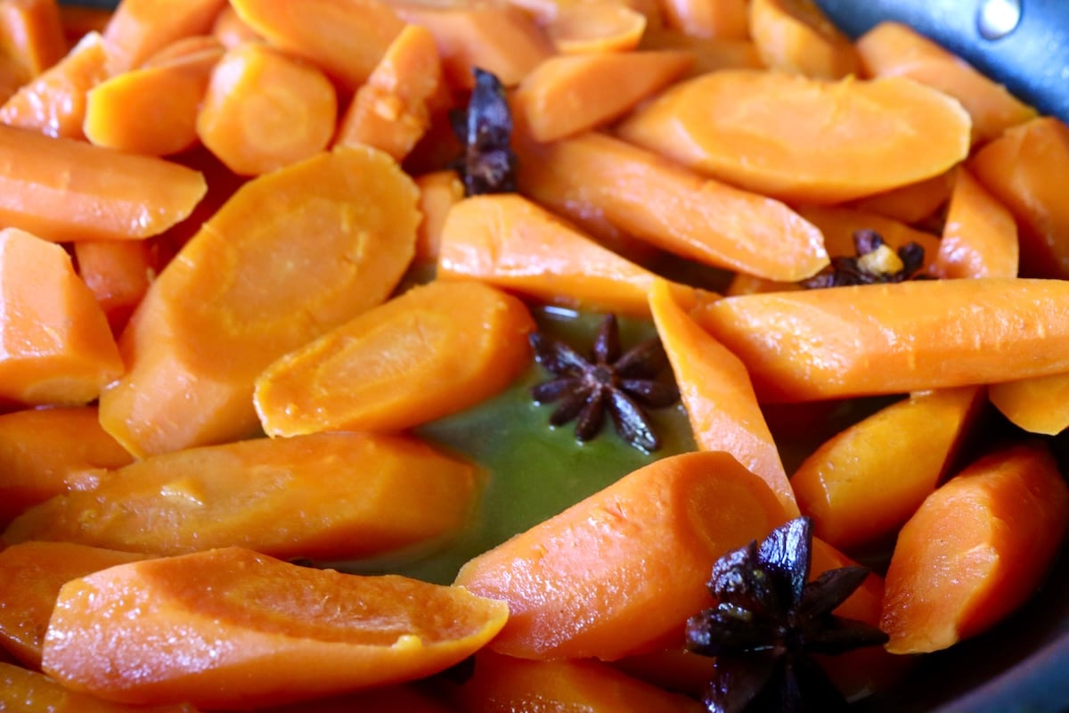 Cooked carrot slices with in a bit of buttery water with several Star Anise, in a sauté pan.