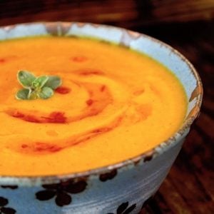 Bright orange Red Kuri Squash pureed soup, in a blue bowl with a small oregano leaf on top.