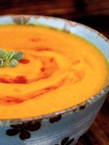 Bright orange Red Kuri Squash pureed soup, in a blue bowl with a small oregano leaf on top.