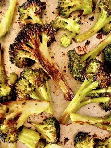 Sheet pan full of super charred broccoli cut into bite-sized pieces.