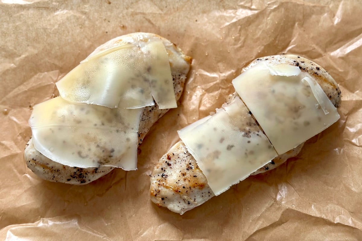 Two grilled chicken breasts with thin slices of melted cheese on top.