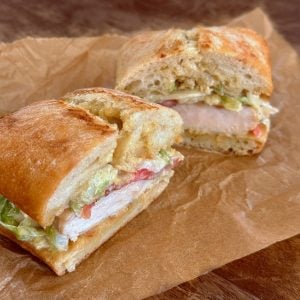 Chicken sandwich cut in half on wrinkled parchment paper.