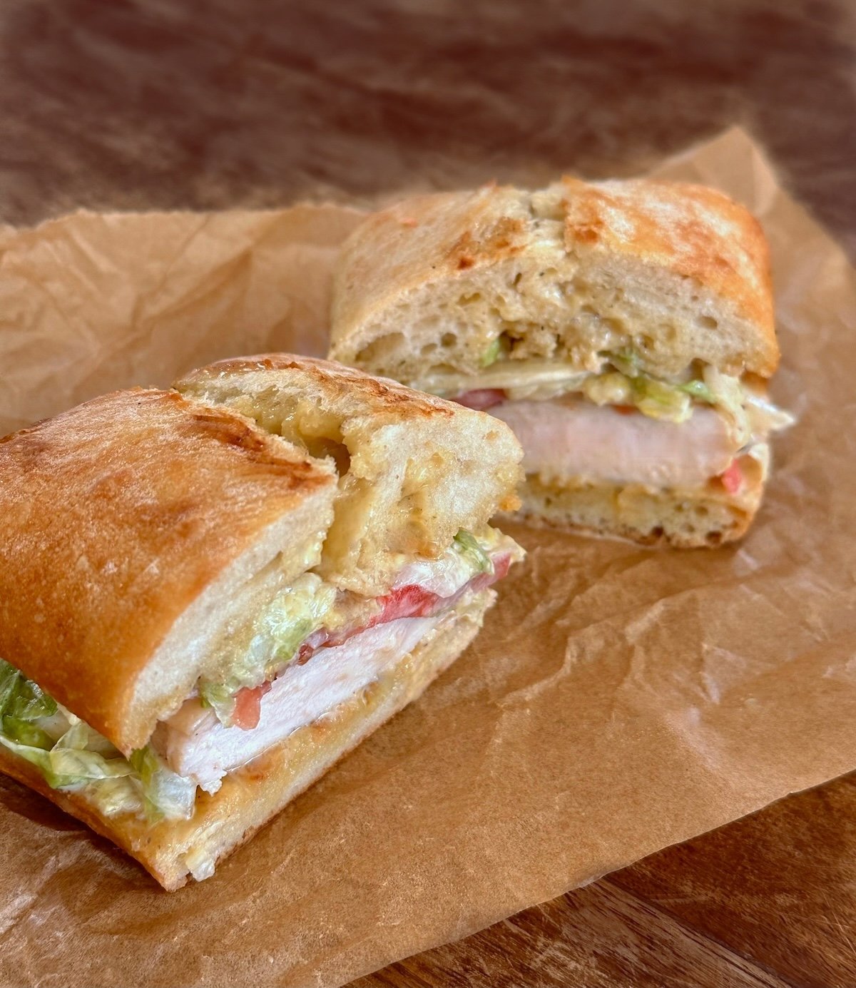 Chicken sandwich cut in half on wrinkled parchment paper.