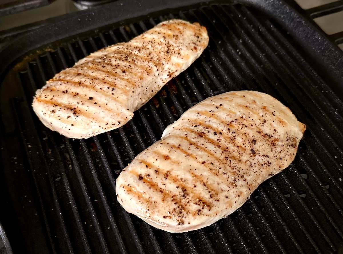 Two chicken breasts with grill marks on a stovetop grill.