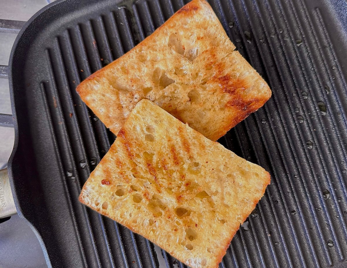 Two halves of a square bun with grill marks on a stovetop grill.