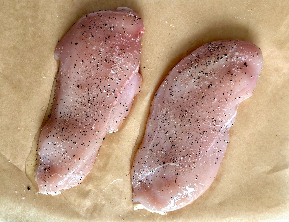 Two raw chicken breasts sprinkled with salt and pepper.