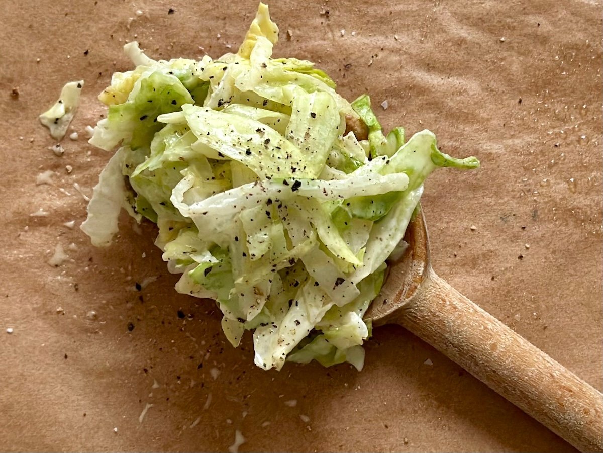 Wooden spoon holding shredded lettuce with ground black pepper.