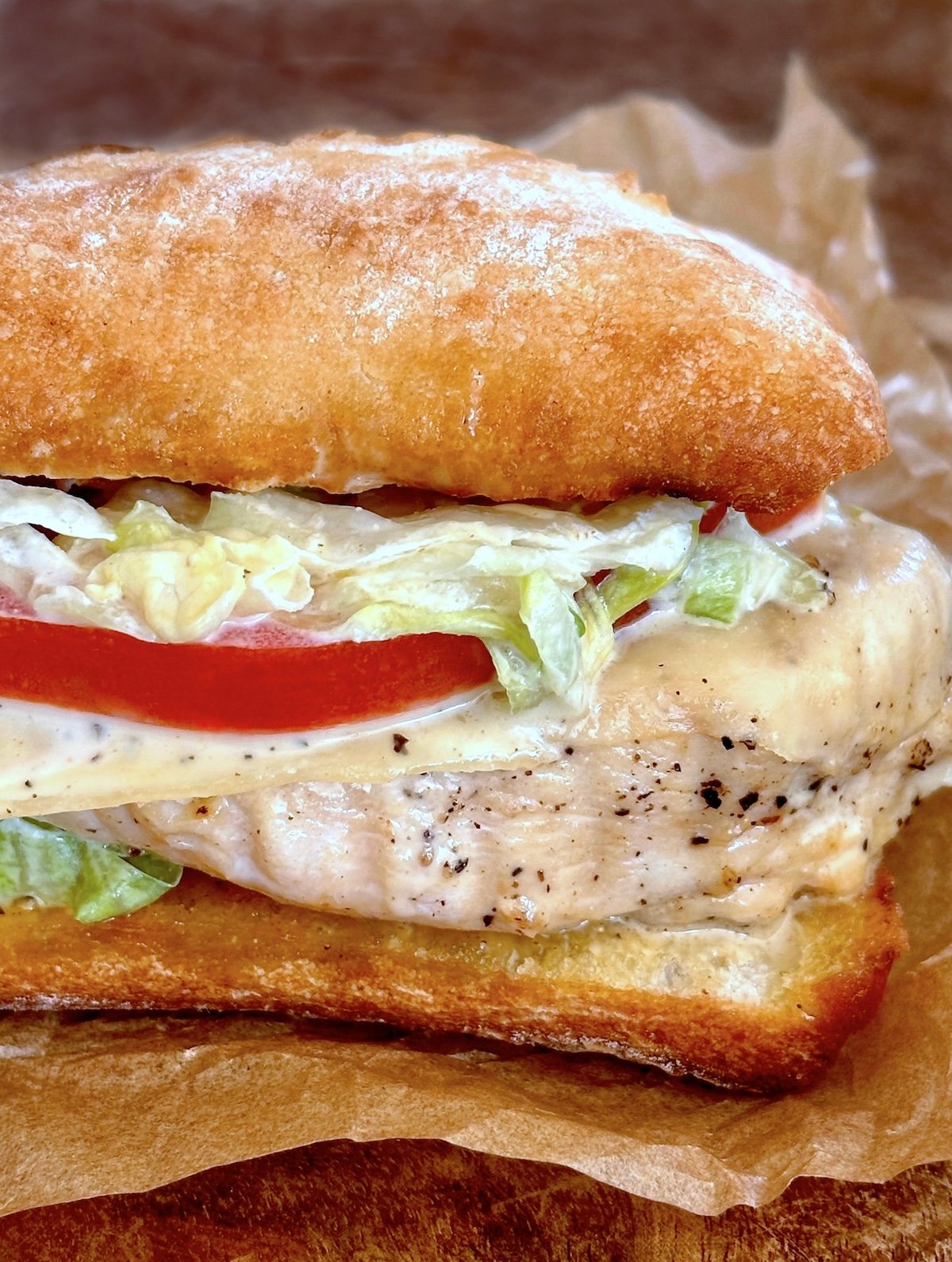 Close up of chicken sandwich with tomato slice and shredded lettuce.