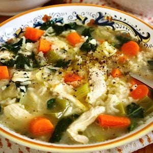 Italian yellow-edged bowl full with chicken and rice soup with carrot slices.