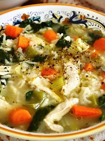 Italian yellow-edged bowl full with chicken and rice soup with carrot slices.