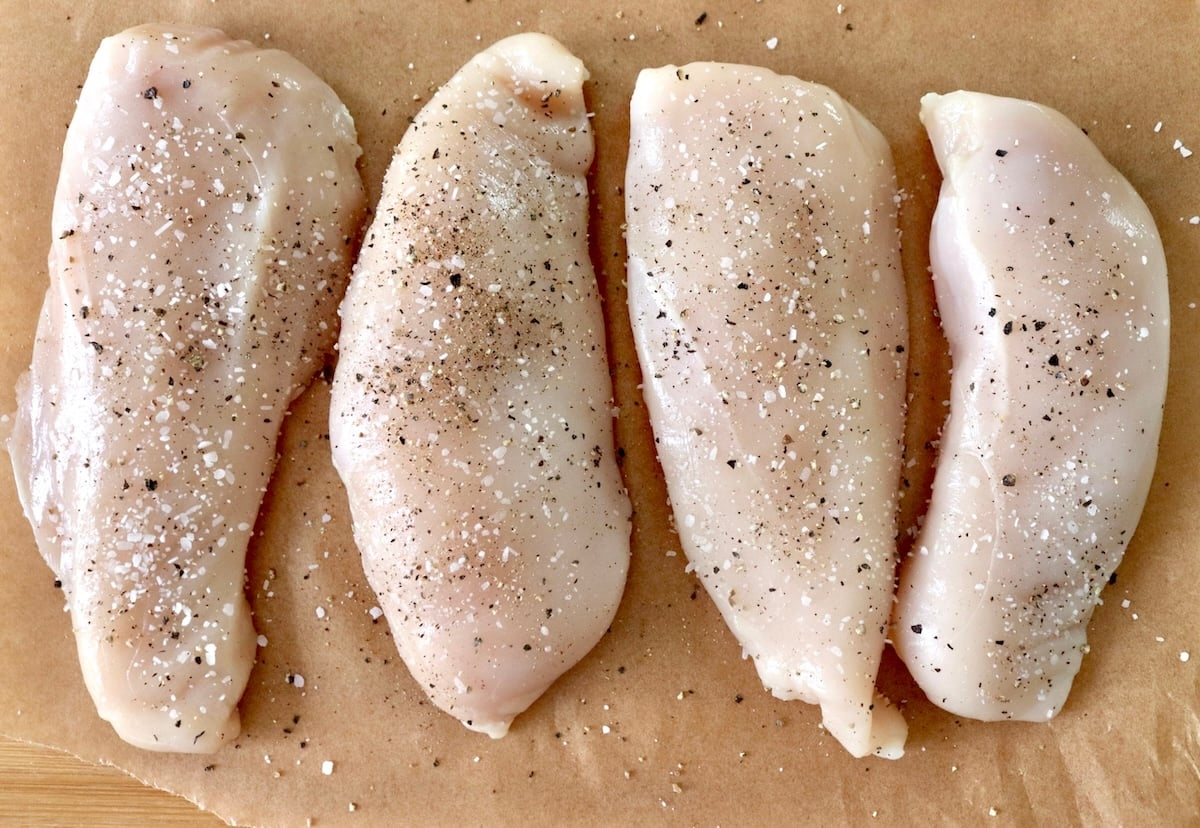 4 chicken breasts with sprinkled with salt and pepper on a piece of parchment paper.