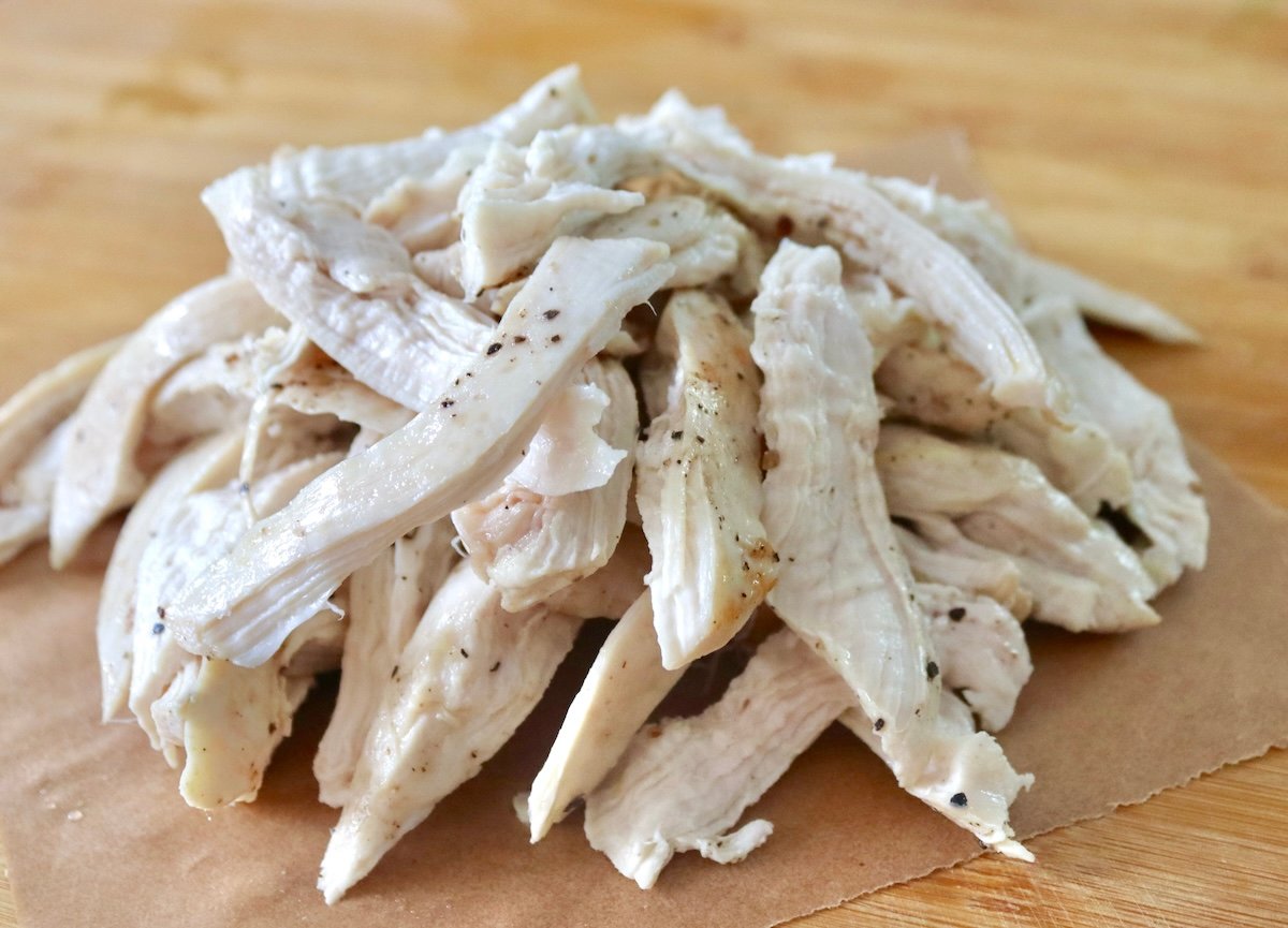 Pile of shredded chicken on a piece of parchment paper.