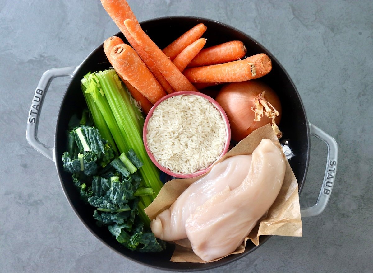 Ingredients for Chicken and Rice Soup including carrots, celery, kale, onion, chicken and rice - all in a Dutch oven.