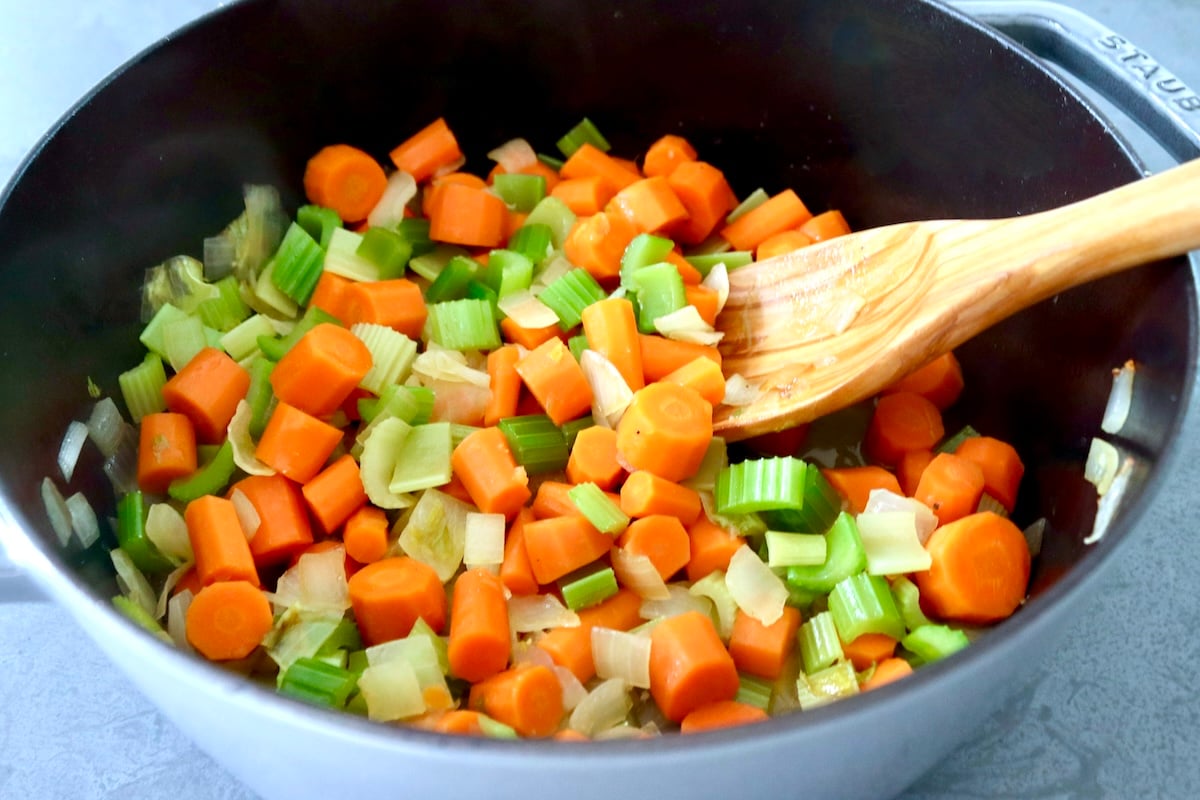 Steamed chopped carrots, celery and onion in a Dutch oven with a wooden spoon.