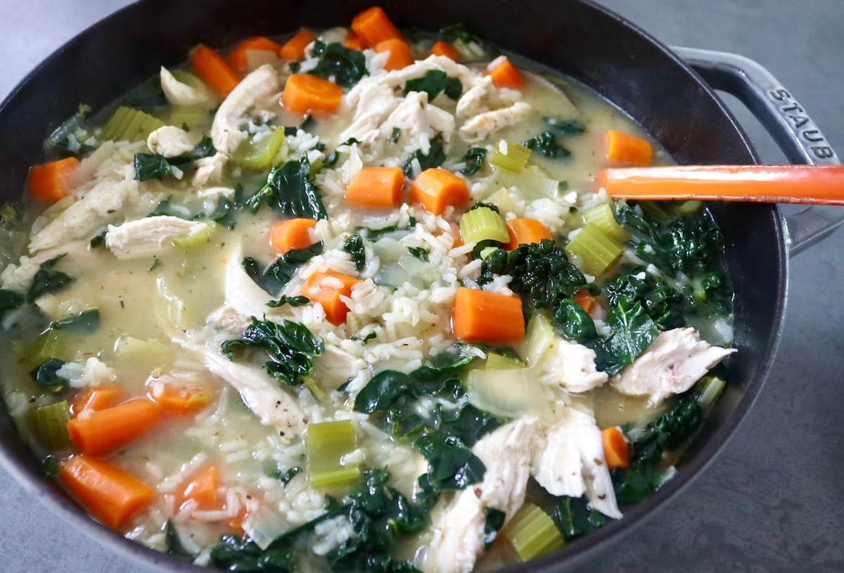 Chicken soup with kale, chicken broth and carrots in pot.