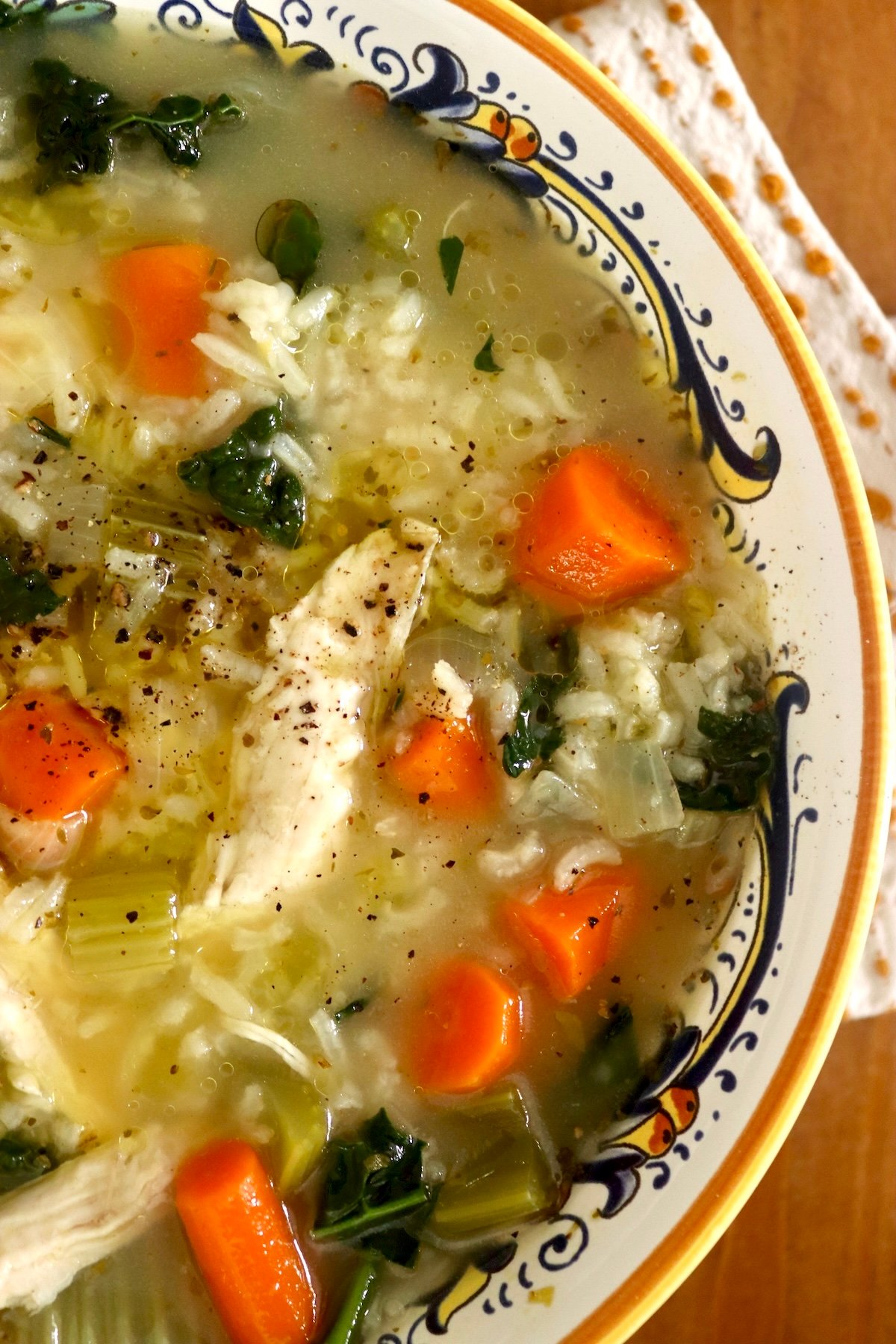 Close up of a old-rimmed Italian bowl with chicken rice soup with carrots and kale.