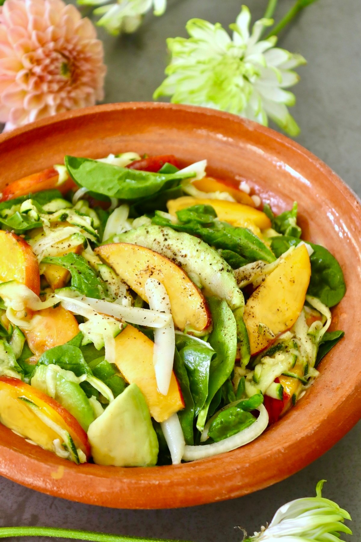 Peach-Avocado-Salad-with-Zucchini Terra cotta bowl with peach avocado salad and fresh flowers behind it.