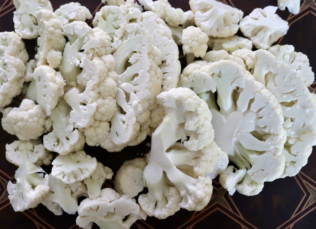 Thick cauliflower slices on a dark wood cutting board.