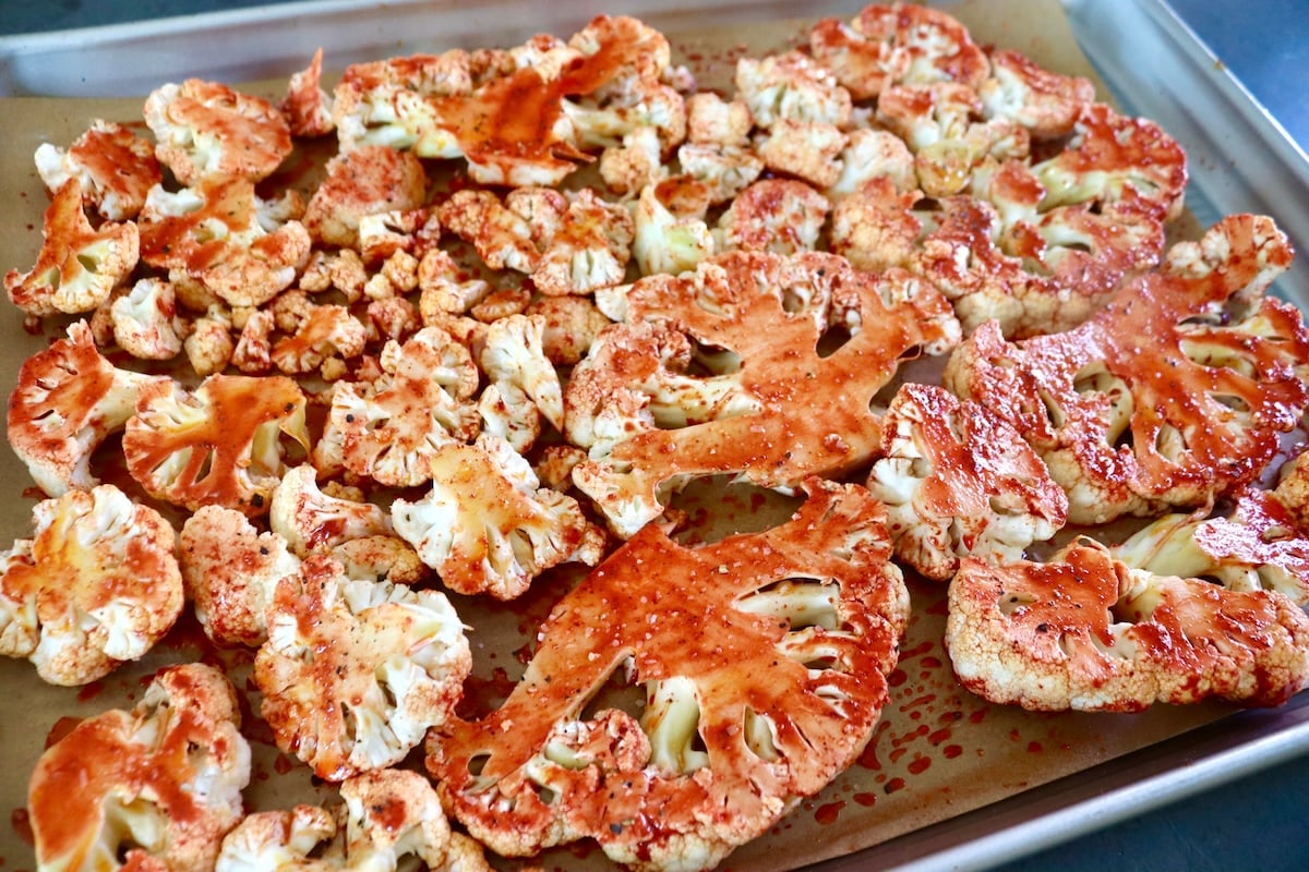 Thick cauliflower slices with red sauce - achiote - on them,on a parchment-lined sheet pan.