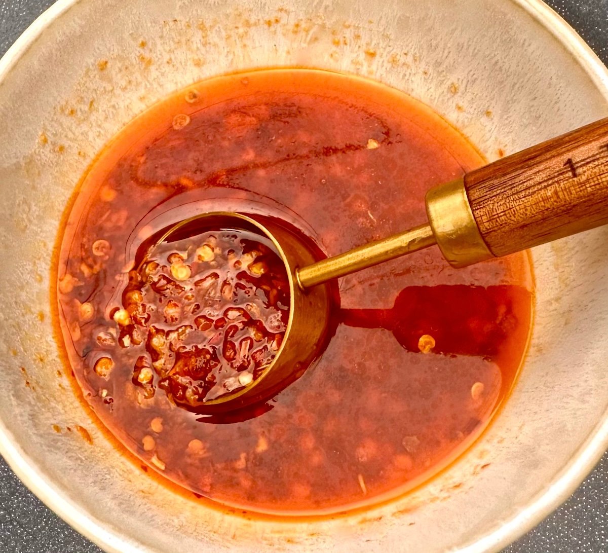 Hot honey with bits of chilies in a cream-colored bowl with a tablespoon.