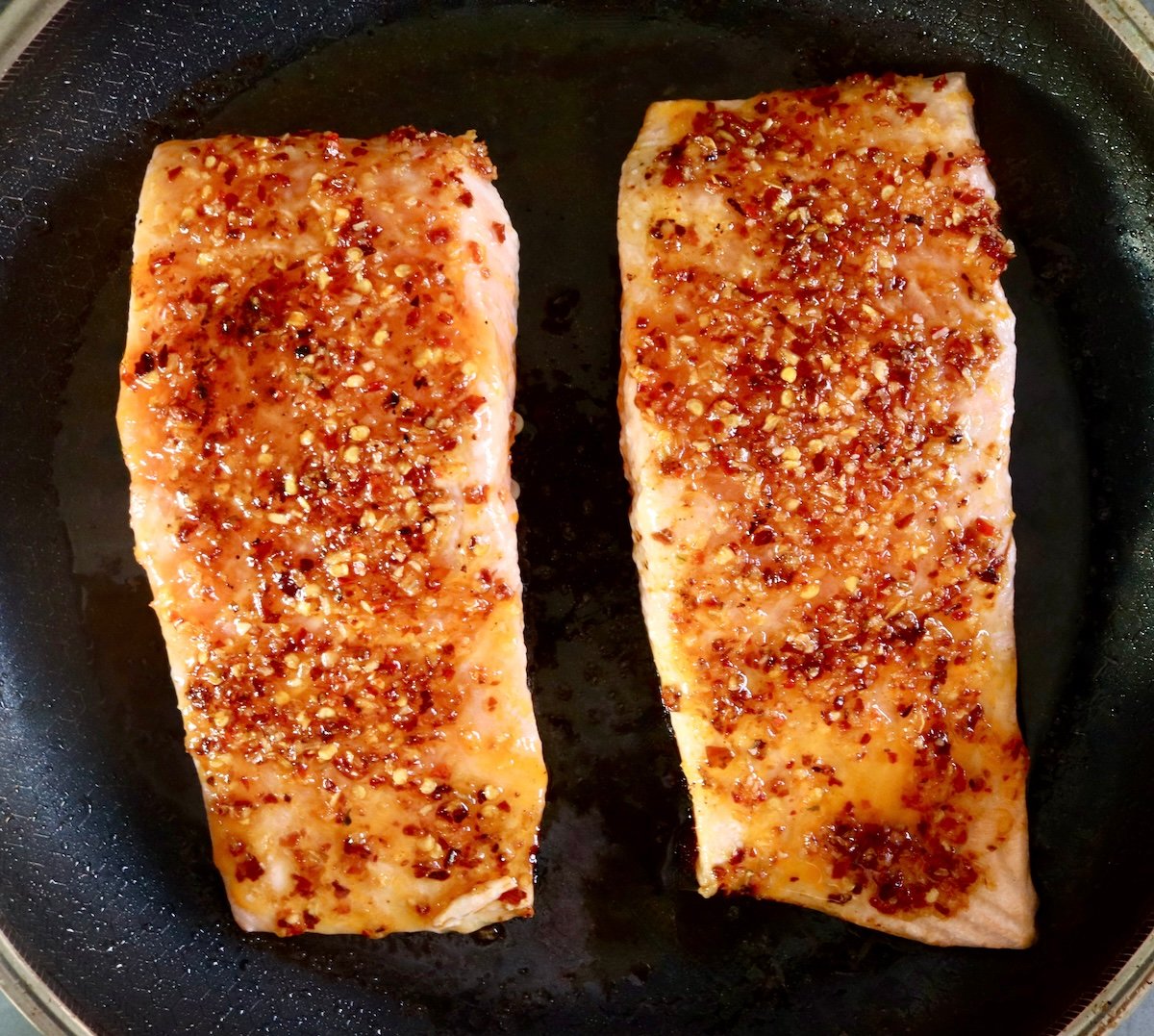 2 cooked hot honey coated salmon fillets in a pan.