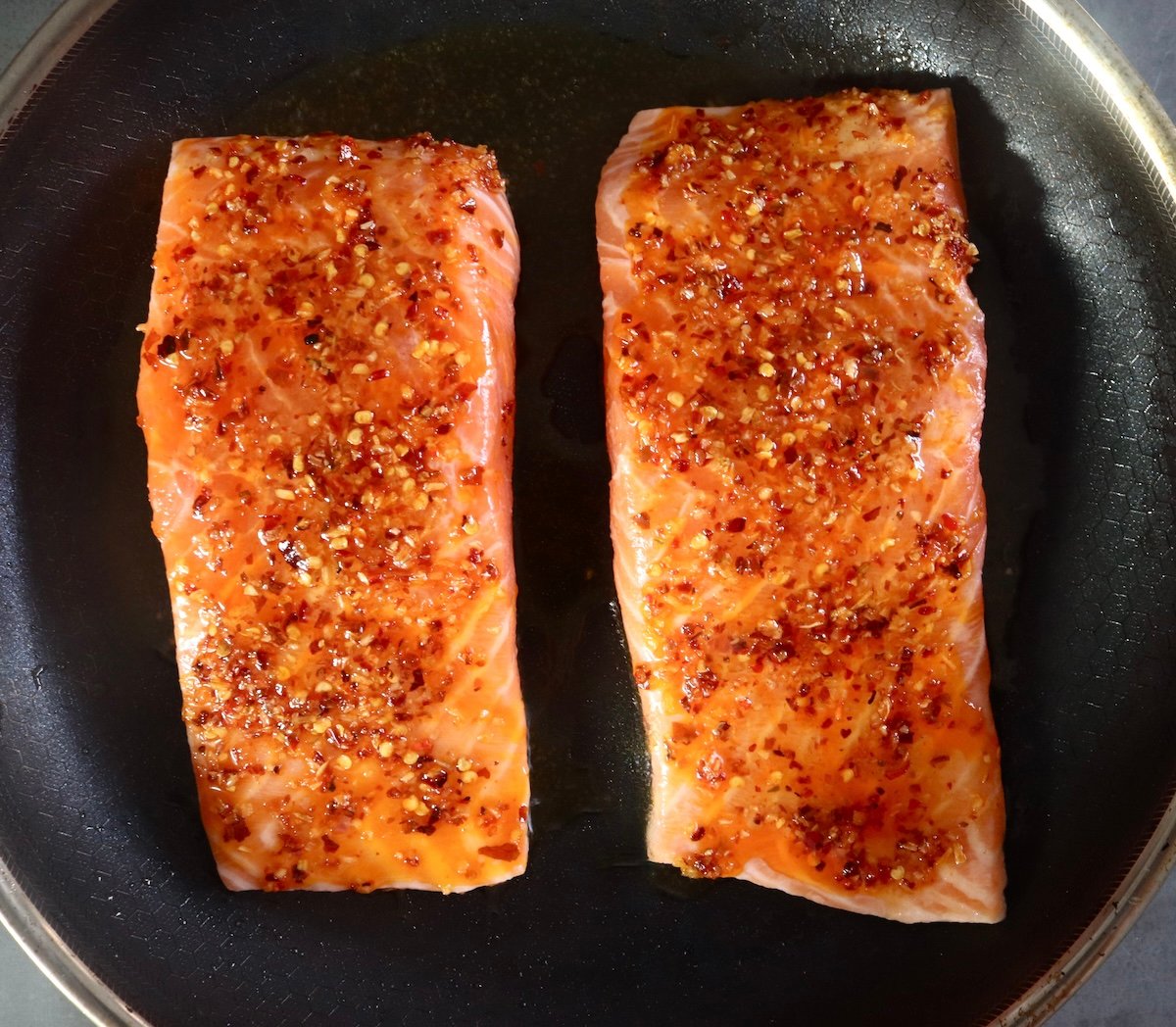 2 raw hot honey coated salmon fillets in a pan.