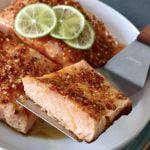 Salmon with chili crunch-honey mixture on top and half of one being held up with a metal spatula.