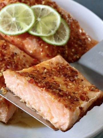 Salmon with chili crunch-honey mixture on top and half of one being held up with a metal spatula.