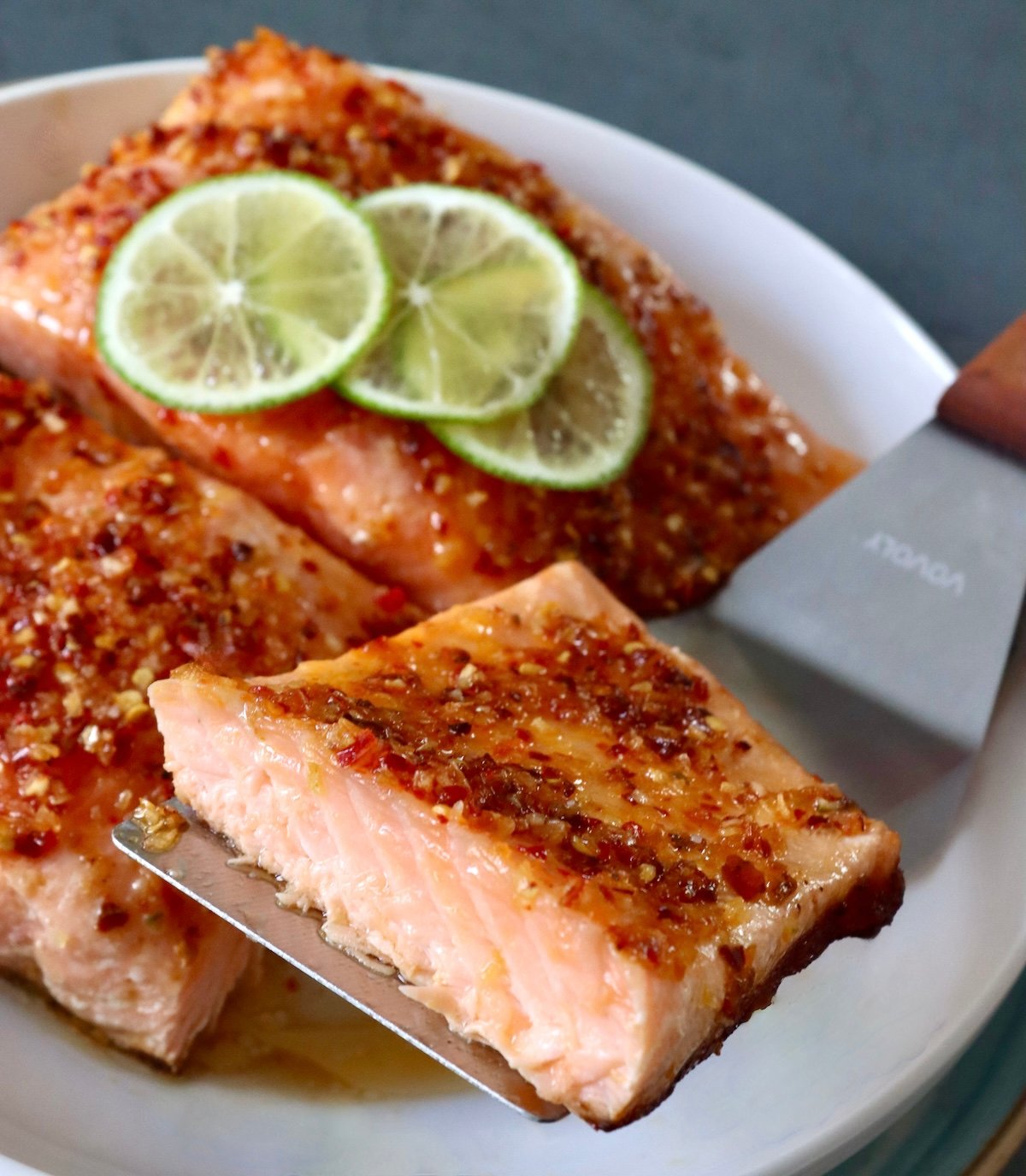Salmon with chili crunch-honey mixture on top and half of one being held up with a etal spatula.