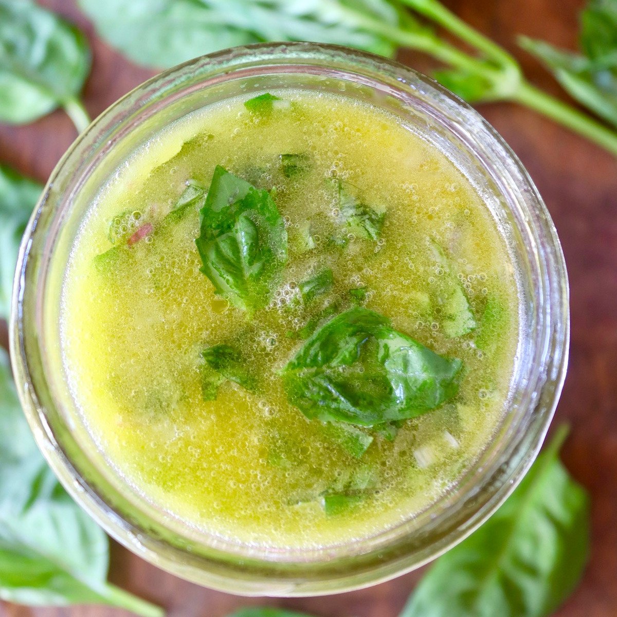 Top view of an open jar of lemon basil salad dressing with fresh basil leave around it.