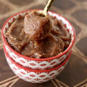Date butter in a red-rimmed bowl on a dark wood cutting board, with a tiny gold spoon.